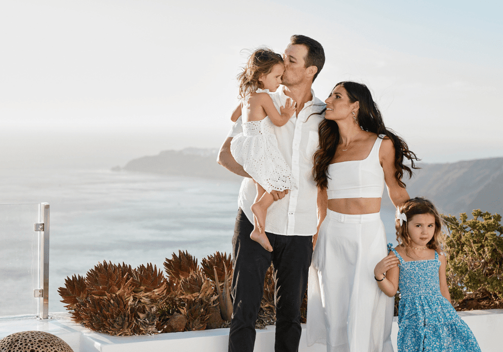 A joyful family poses on a balcony at Erossea Villa Santorini, capturing a moment with the ocean as their backdrop