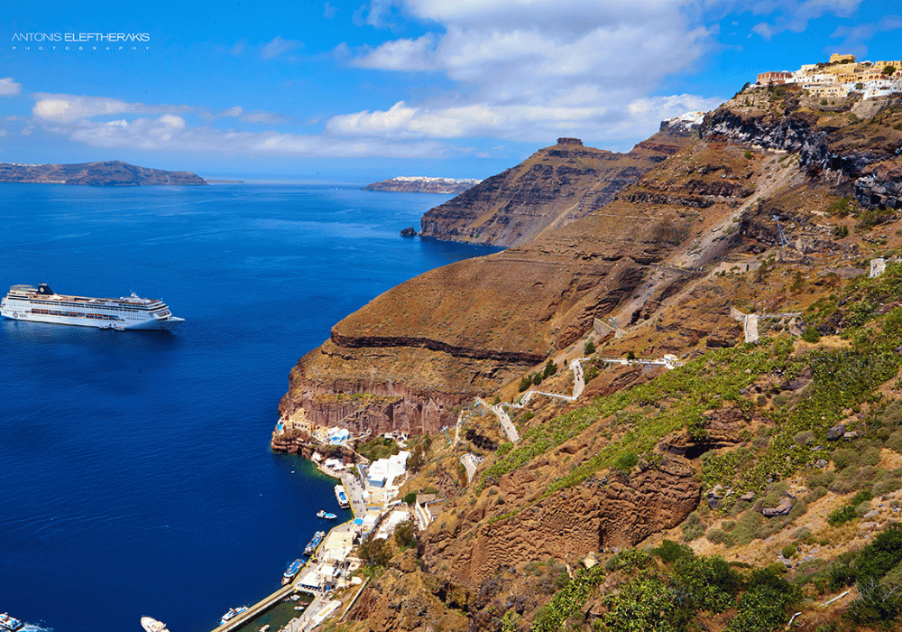 A large cruise ship glides through the ocean near the stunning cliffs of Santorini Fira, showcasing a picturesque view