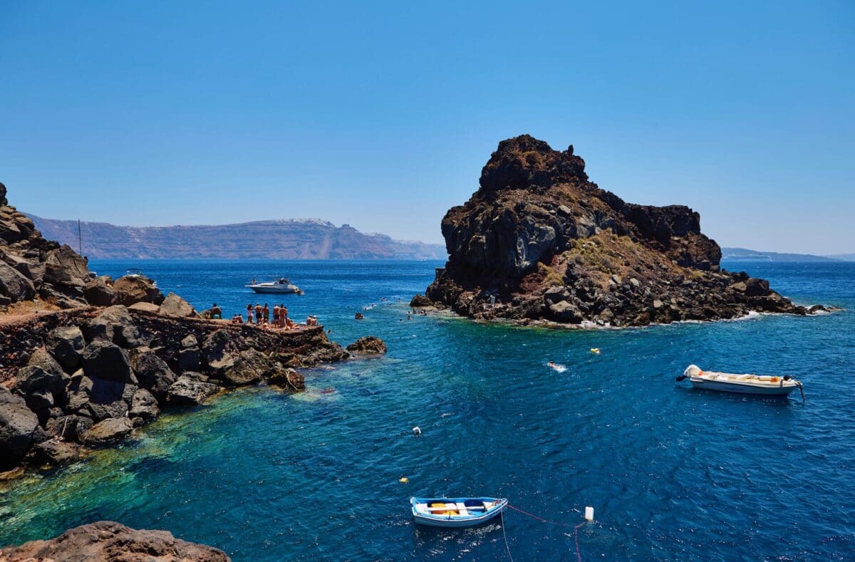 Ammoudi Bay aerial view with people waiting to cliff jump into the crystal clear blue sea